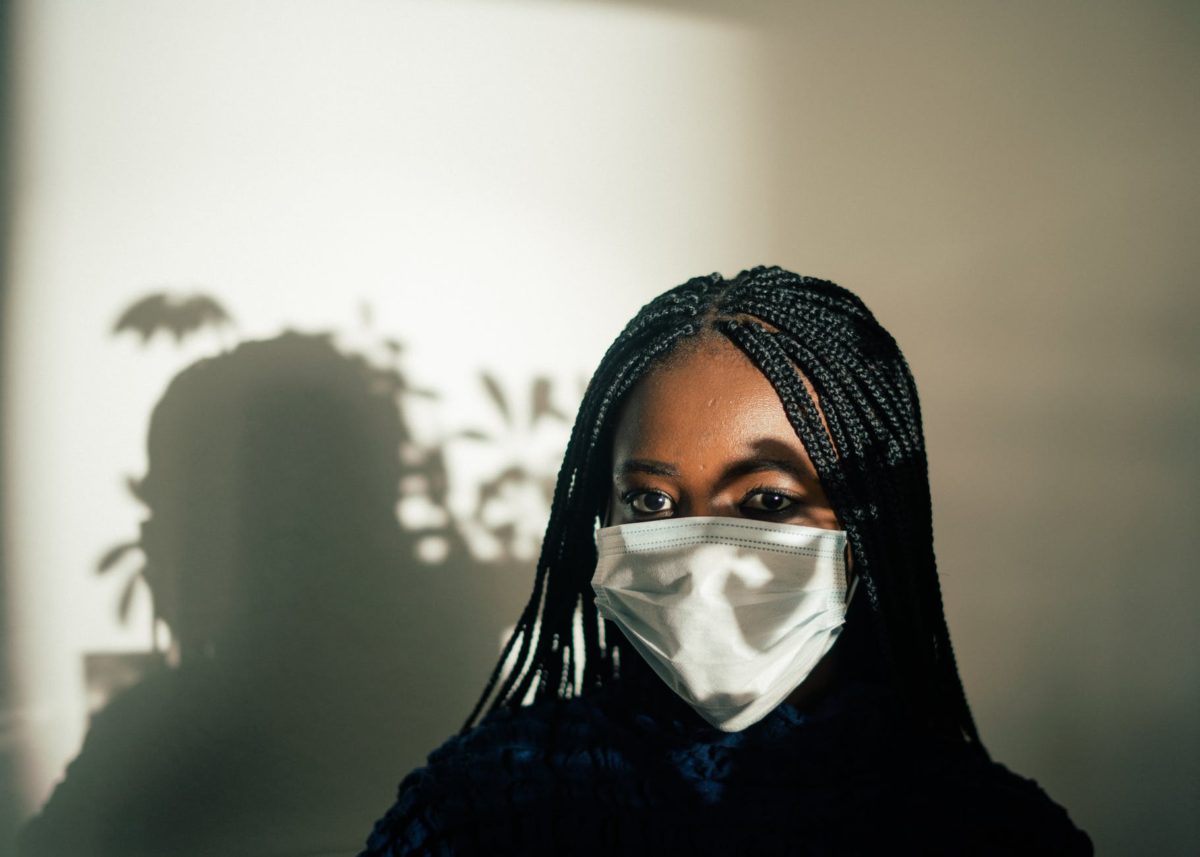 black woman in medical mask against white wall with shadow