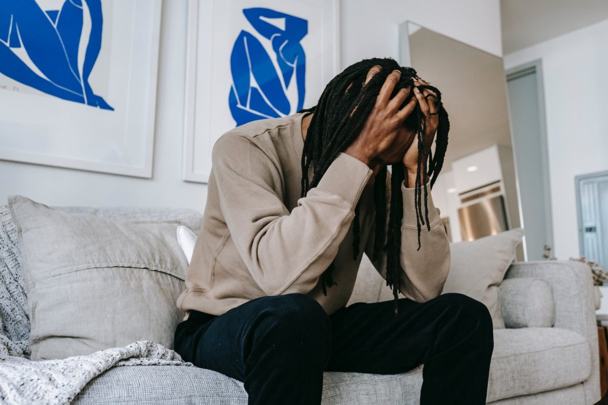 unrecognizable depressed black man touching head on couch at home