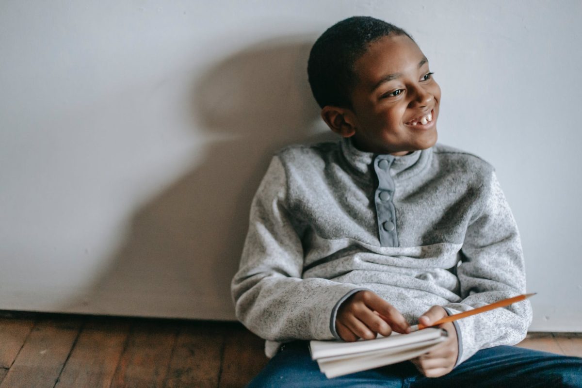 happy african american boy sitting on floor with copybook and pencil