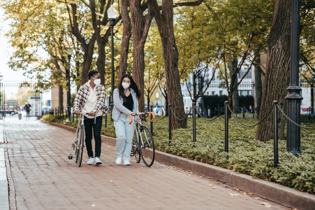 multiethnic friends walking together along park alley with bicycles