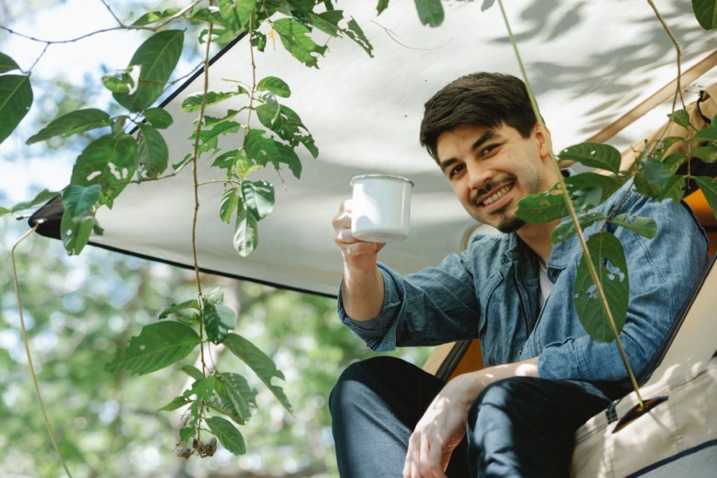 content young man enjoying beverage while recreating in tent during camping