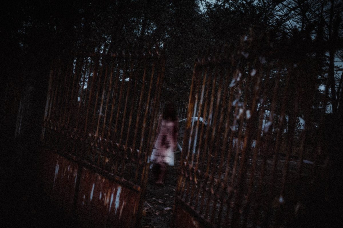 unrecognizable zombie woman walking in park near aged metal fence
