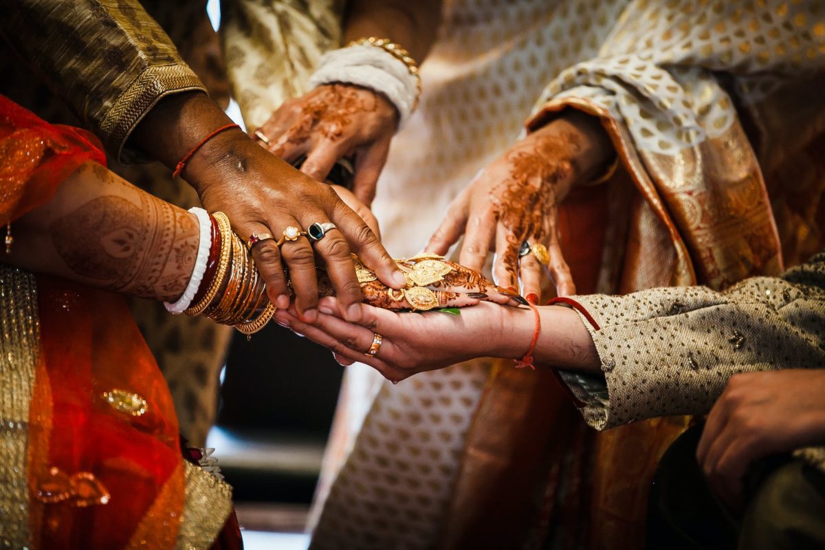 crop ethnic people in traditional outfits putting hands together during wedding ceremony